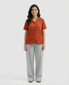 Woman wearing a rust-colored button-up shirt and gray pants on a white background