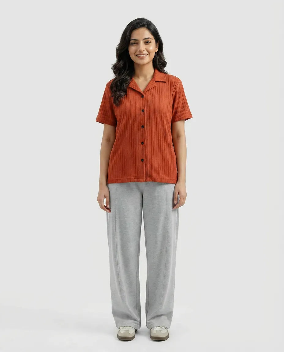 Woman wearing a rust-colored button-up shirt and gray pants on a white background