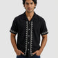Man wearing a black shirt with white embroidery on a gray background