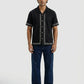 Man wearing a black short-sleeve shirt with white patterns and dark blue jeans on a white background