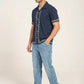 Man wearing a navy blue embroidered shirt and light blue jeans on a white background