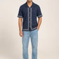 Man wearing a navy blue shirt with white embroidery and light blue jeans on a beige background