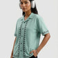 Woman wearing a light green shirt with black embroidery and white headphones on a light gray background