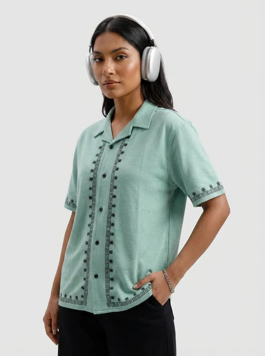 Woman wearing a light green shirt with black embroidery and white headphones on a light gray background