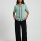 Woman wearing a light green blouse with black pants on a white background