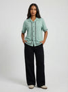 Woman wearing a light green blouse with black pants on a white background